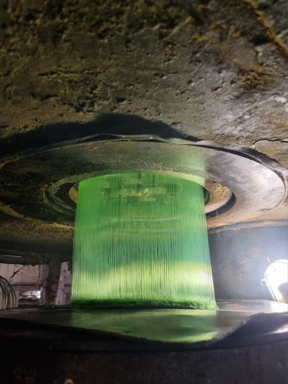 Illuminated circular spinneret plate extruding molten polyester filaments